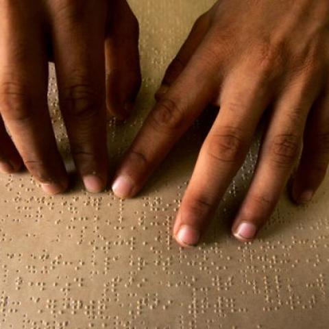 Two hands are reading a braille document in dim lighting