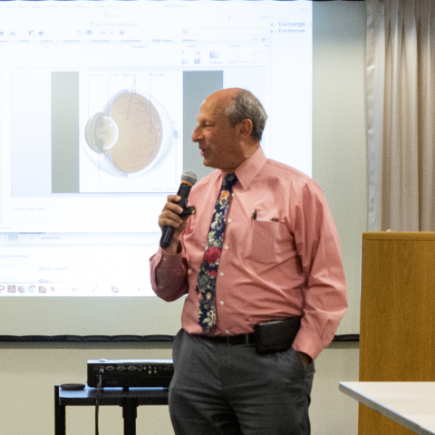 Dr. Fletcher speaking into a microphone in front of an anatomical image of an eye