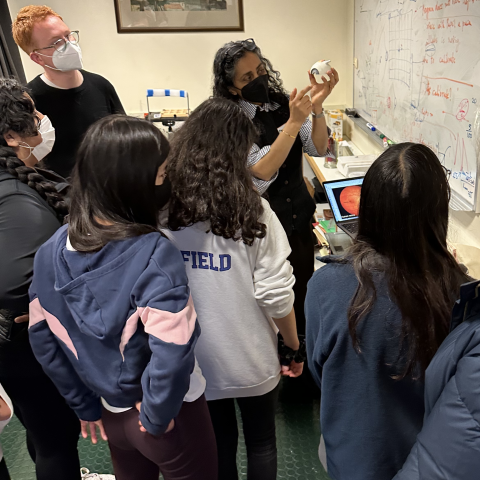 Dr. Verghese demonstrating something at a whiteboard to a group of students