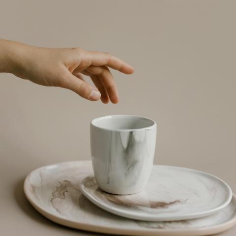 photograph of a person's hand reaching for a cup with a grasp movement that appears to be poorly suited for the task
