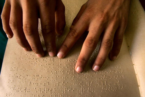 Two hands are reading a braille document in dim lighting