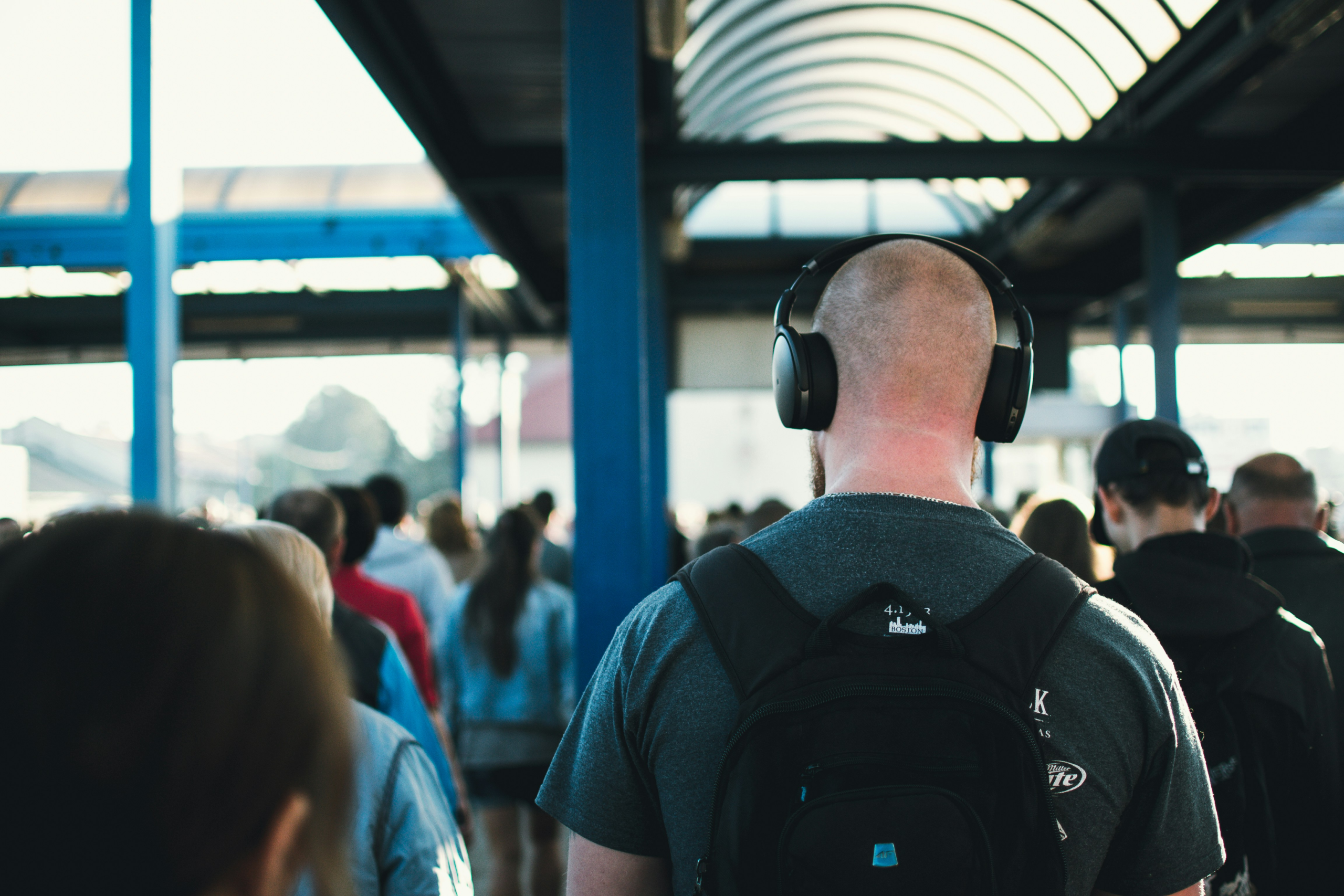 Man in busy train station walking away while wearing headphones
