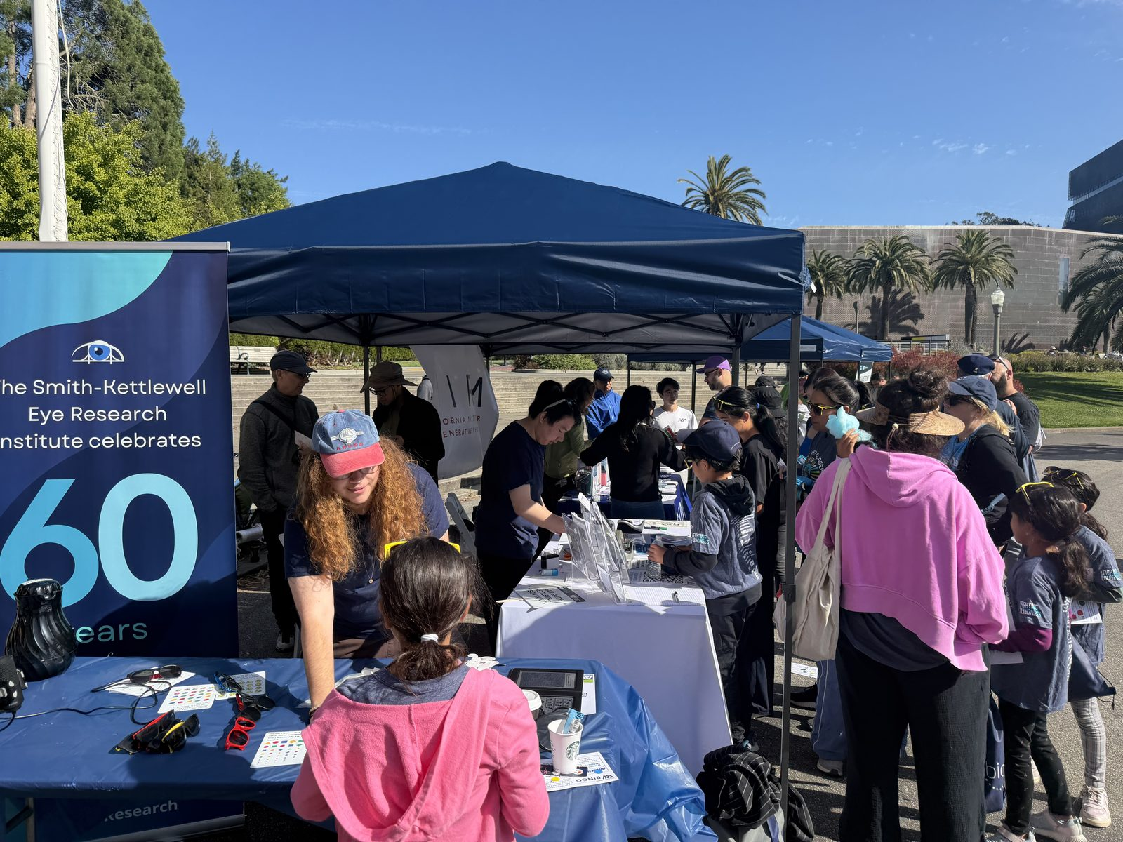 Visitors gather at the Smith-Kettlewell Eye Research Institute booth at VisionWalk 2026, trying vision simulation glasses and low vision demonstrations.