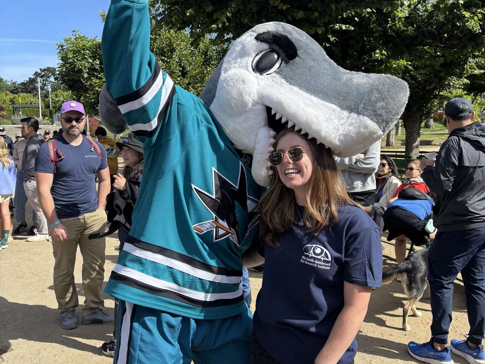 Smith-Kettlewell research intern Alta Knuff poses with SJ Sharkie, the San Jose Sharks mascot, at the 2026 Bay Area VisionWalk in Golden Gate Park.