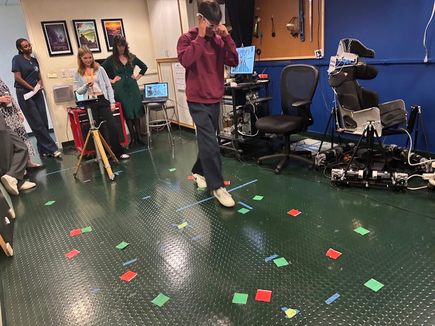 A student wearing vision-simulating glasses walks a marked course during a mobility demonstration.